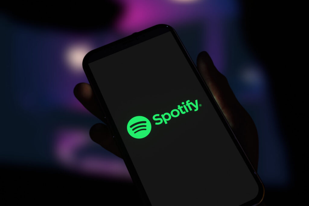 Smartphone displaying the Spotify logo on screen, held in a hand against a dark, blurred background.